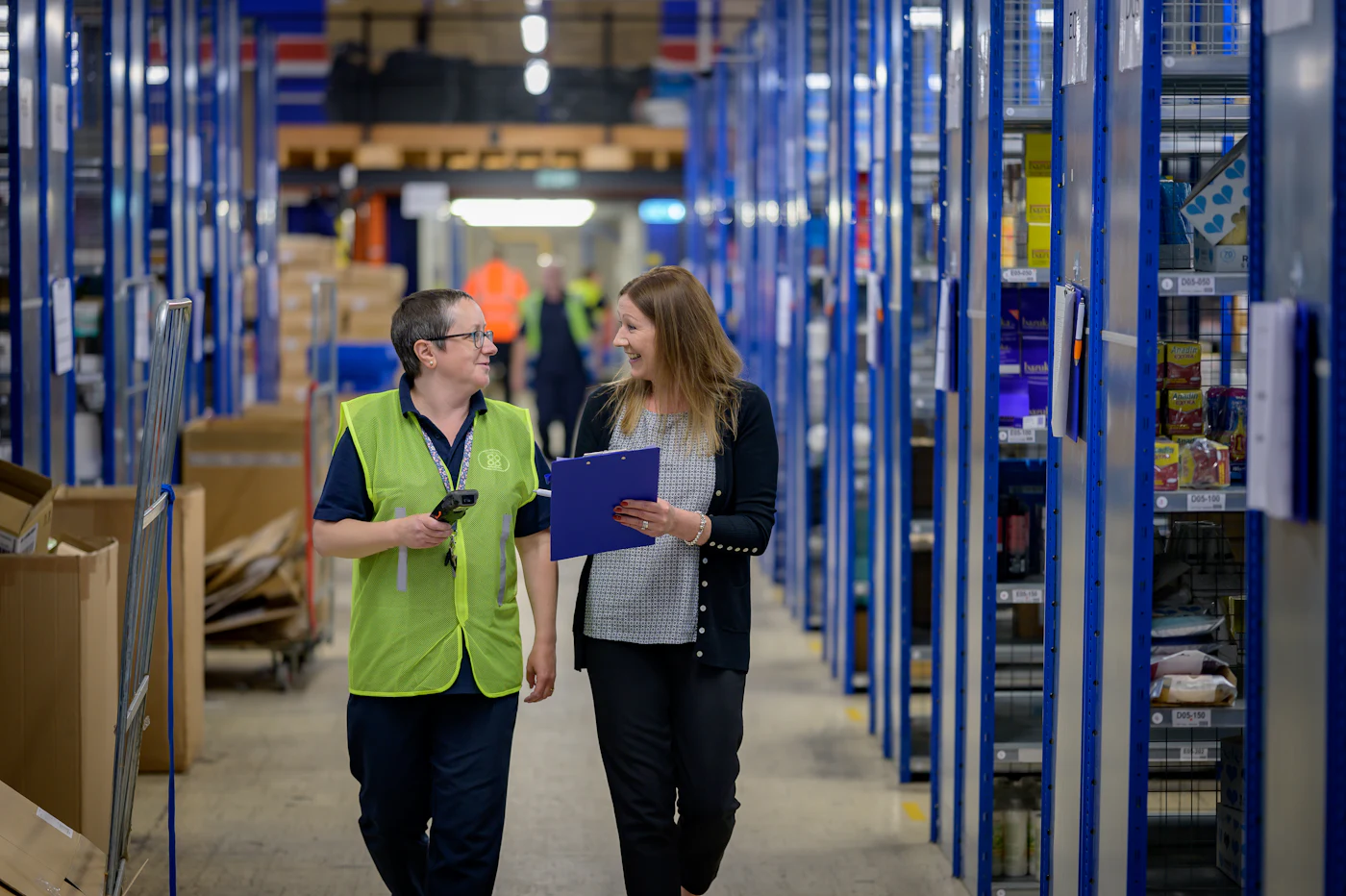 Two operations leads walking a warehouse aisle with a clipboard